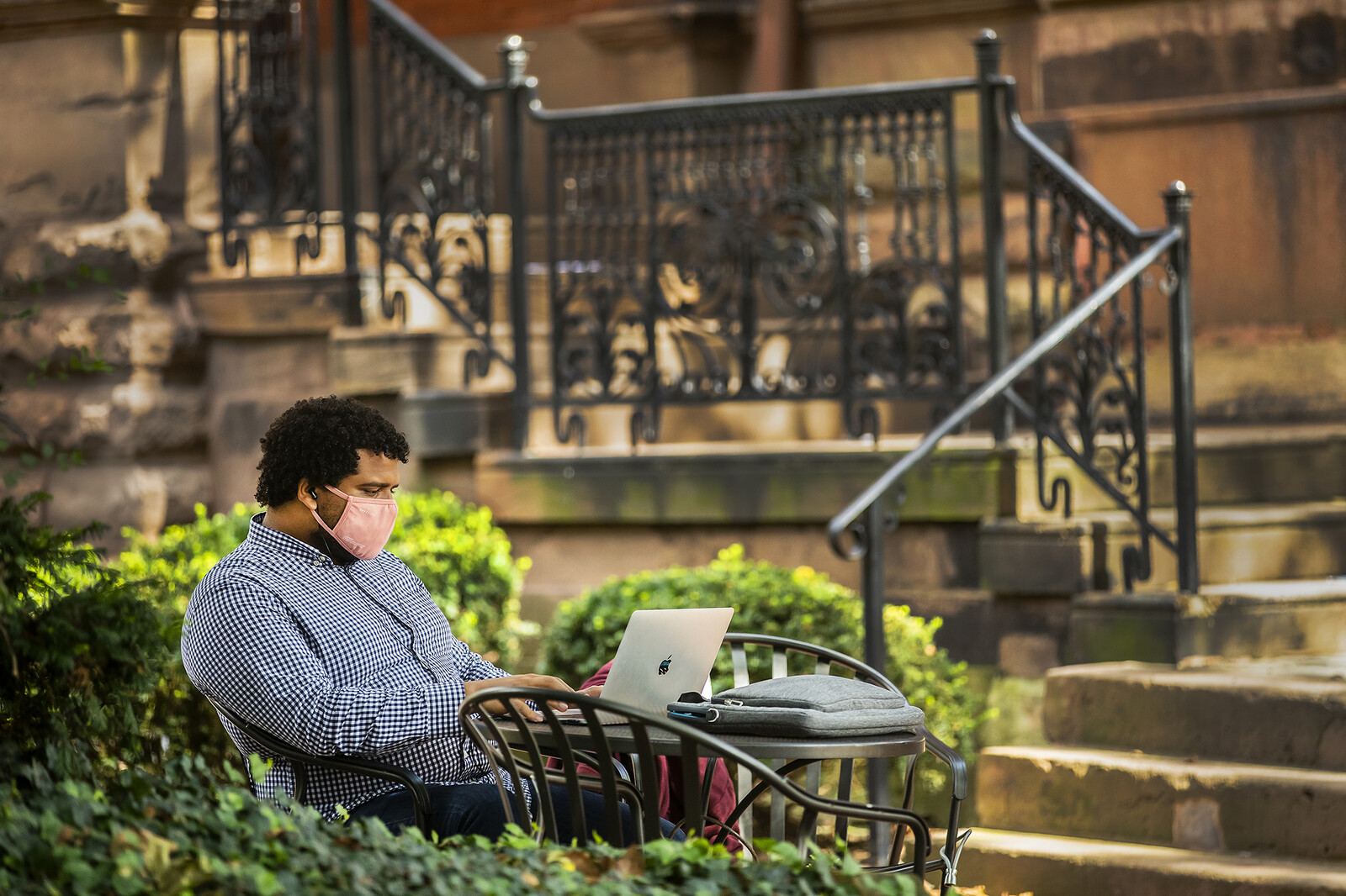student sitting on locust walk on a laptop with mask